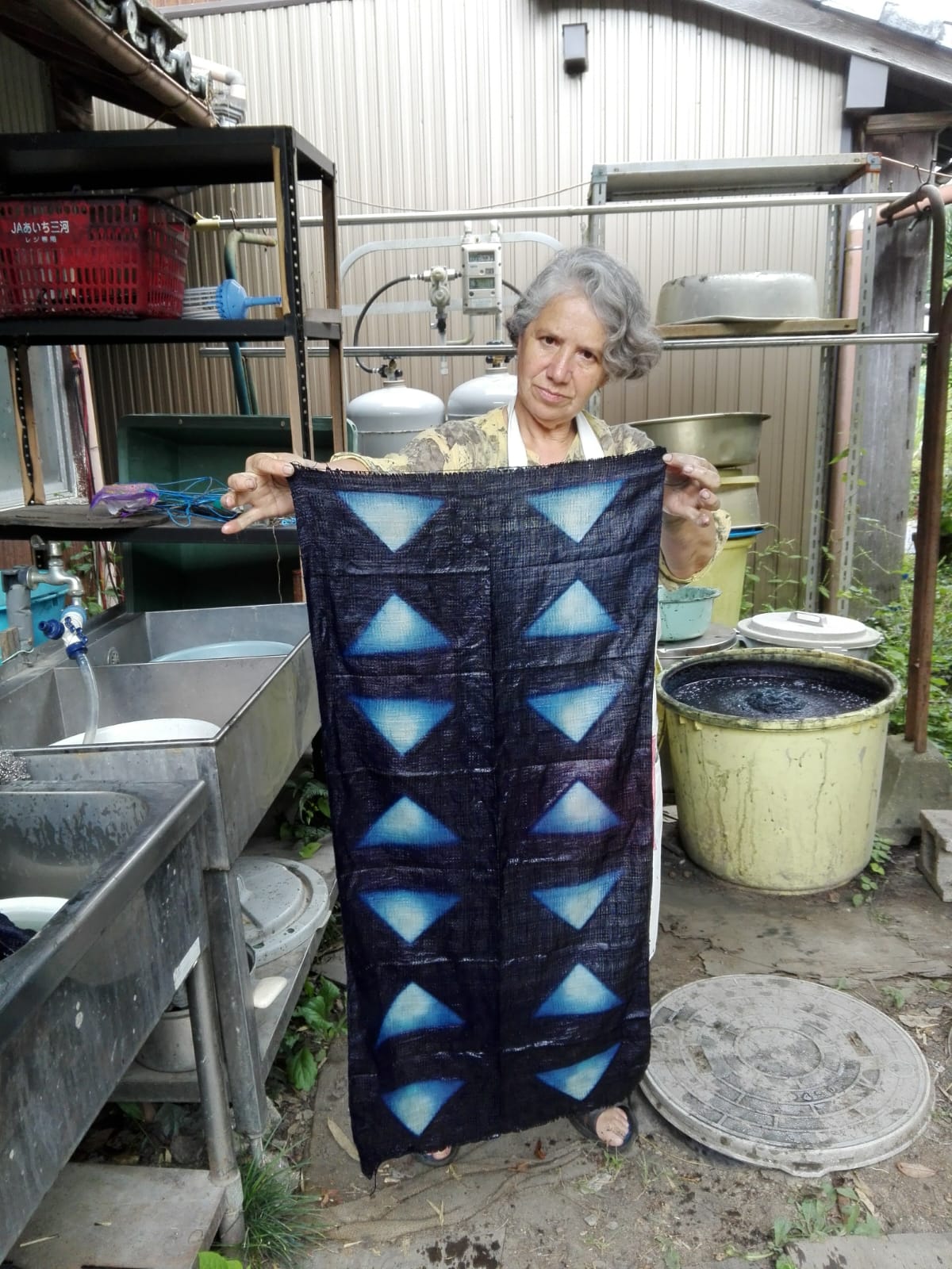 Susana Peñaloza muestra una tela teñida con índigo junto a la tina de fermentación, Okazaki, Japón